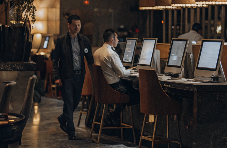 Hotel restaurant staff working on computers in a modern lobby with guests in the background